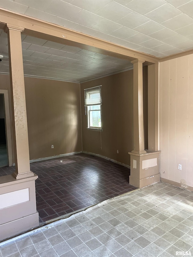 spare room with wooden walls, ornamental molding, and ornate columns