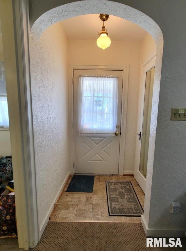 doorway featuring arched walkways, a textured wall, and baseboards