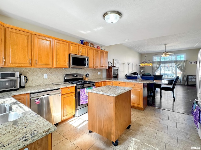 kitchen featuring a center island, stainless steel appliances, backsplash, light stone countertops, and a peninsula