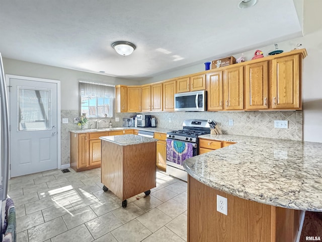 kitchen featuring light stone countertops, appliances with stainless steel finishes, backsplash, and a center island