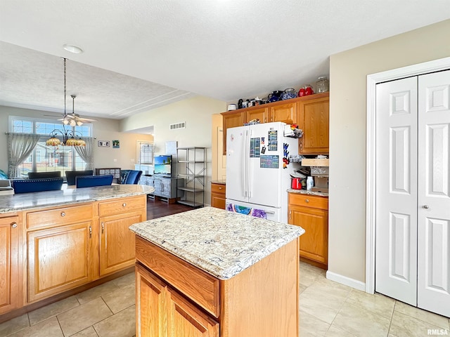 kitchen with light stone countertops, a center island, open floor plan, freestanding refrigerator, and brown cabinets