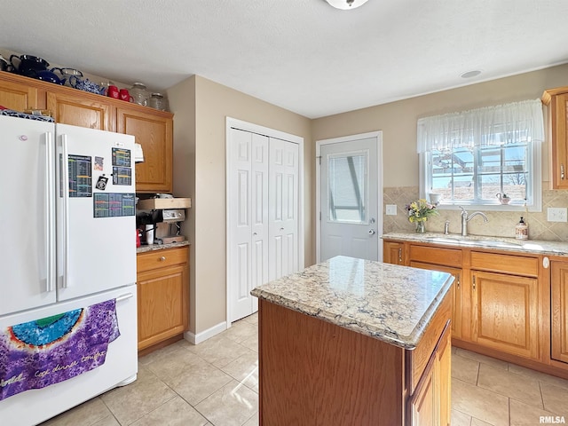 kitchen with a center island, tasteful backsplash, brown cabinetry, freestanding refrigerator, and a sink