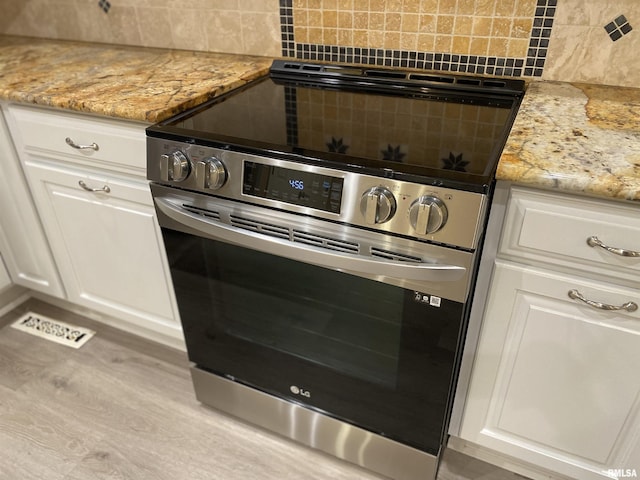 kitchen featuring white cabinetry, stainless steel electric range oven, light stone countertops, and decorative backsplash