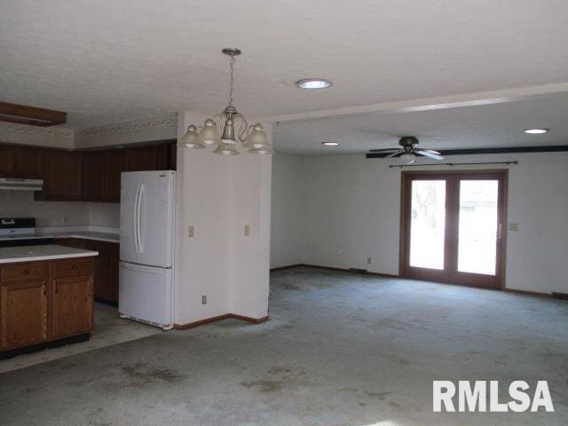 kitchen featuring stove, decorative light fixtures, ceiling fan with notable chandelier, white fridge, and light colored carpet