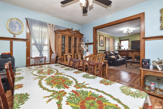 dining room with ceiling fan with notable chandelier, a textured ceiling, dark hardwood / wood-style floors, and a fireplace