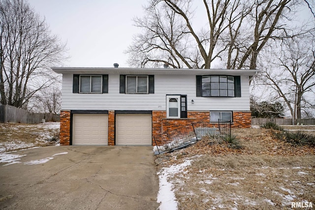 bi-level home featuring a garage, brick siding, driveway, and fence