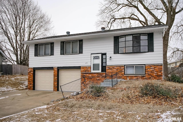 raised ranch with driveway, brick siding, an attached garage, and fence