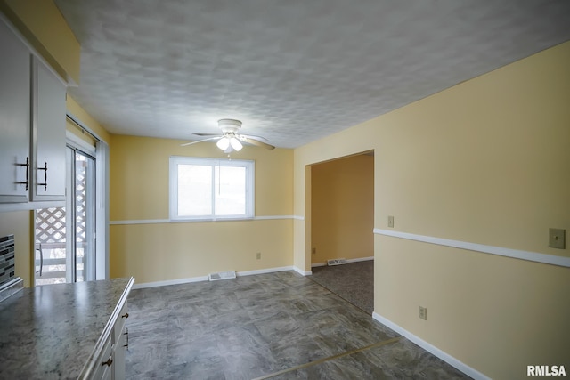 interior space featuring visible vents, a ceiling fan, white cabinets, a textured ceiling, and baseboards