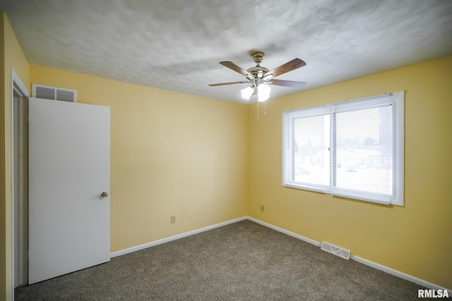 unfurnished room with a ceiling fan, dark colored carpet, visible vents, and baseboards