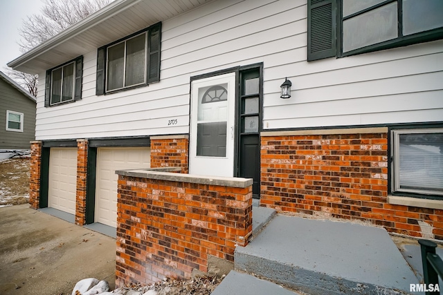 entrance to property featuring concrete driveway, brick siding, and an attached garage