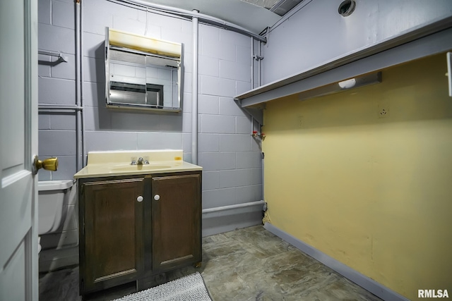 bathroom featuring vanity, toilet, and concrete block wall