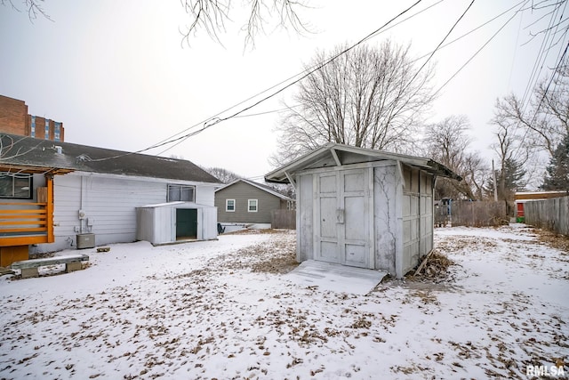 snow covered structure with a storage shed, an outbuilding, and central air condition unit