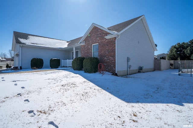 view of snow covered exterior with a garage, brick siding, and fence