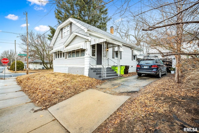 bungalow featuring driveway, a chimney, and roof with shingles