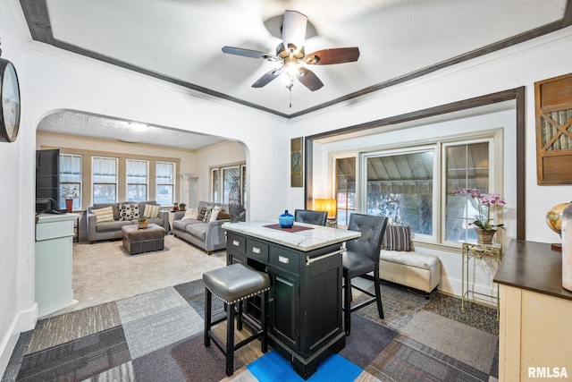 dining area featuring baseboards, arched walkways, a ceiling fan, ornamental molding, and dark colored carpet