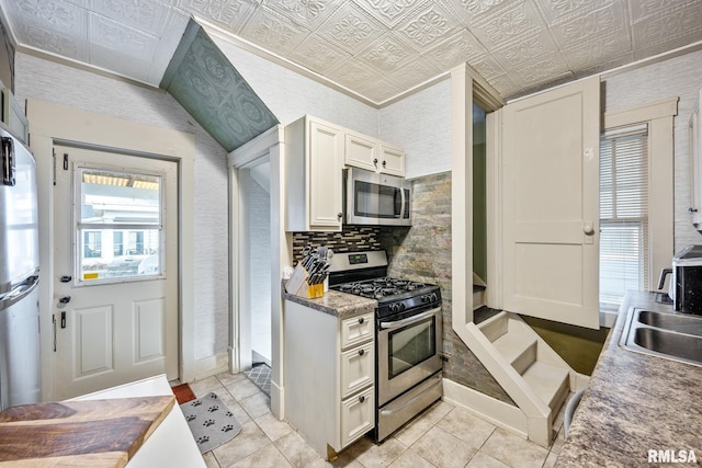 kitchen with decorative backsplash, white cabinets, an ornate ceiling, appliances with stainless steel finishes, and a sink