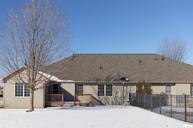 snow covered back of property featuring a shingled roof, fence, and a wooden deck