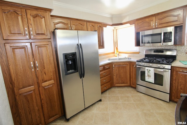 kitchen featuring brown cabinets, crown molding, light countertops, appliances with stainless steel finishes, and a sink