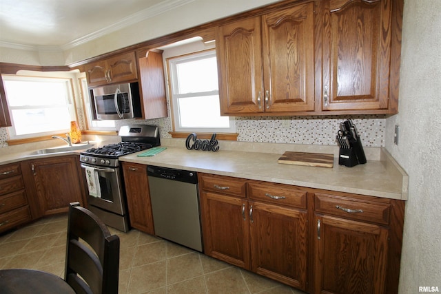 kitchen with appliances with stainless steel finishes, ornamental molding, a sink, light countertops, and backsplash