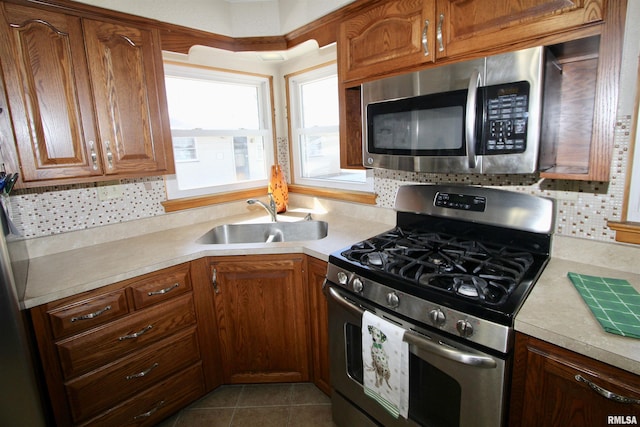 kitchen with appliances with stainless steel finishes, brown cabinetry, light countertops, and a sink