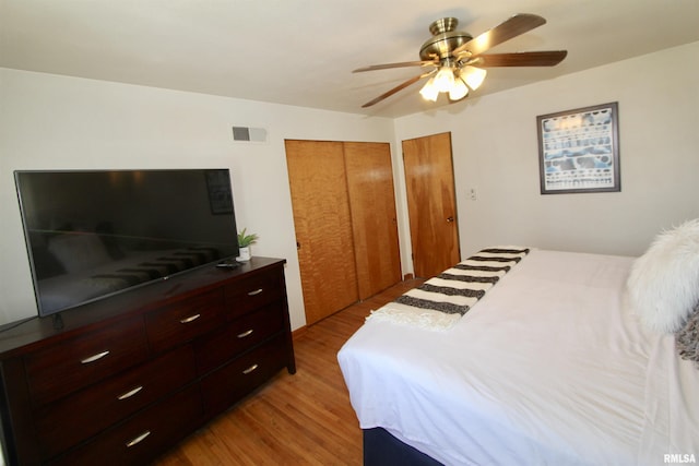 bedroom with light wood finished floors, visible vents, a ceiling fan, and two closets