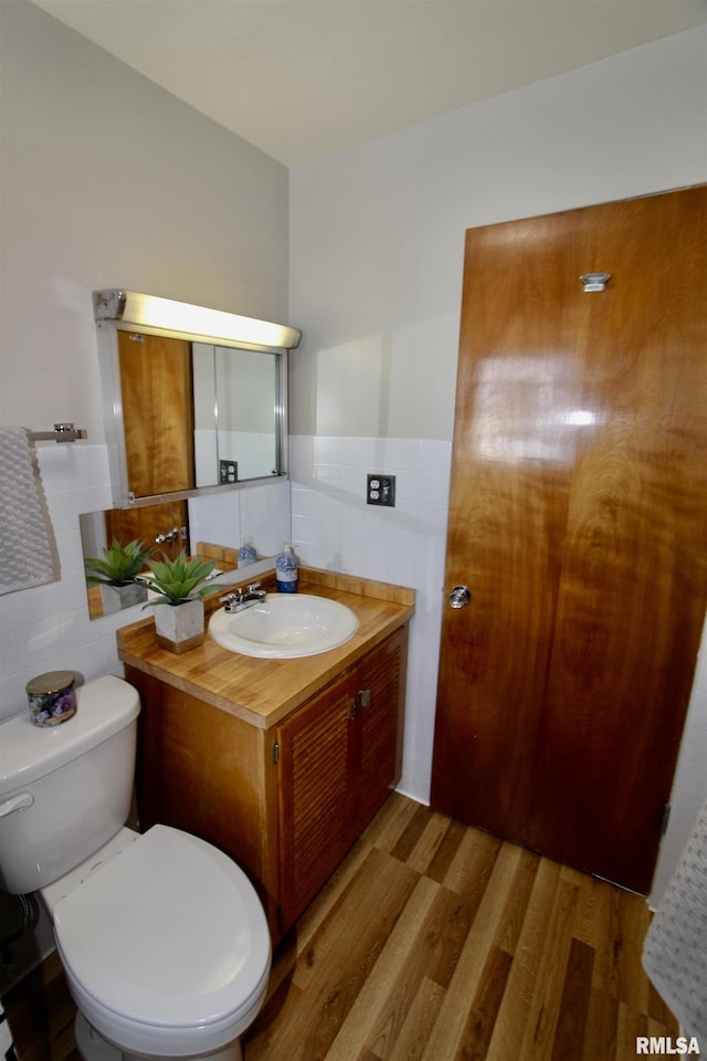 half bathroom with vanity, wainscoting, wood finished floors, and tile walls