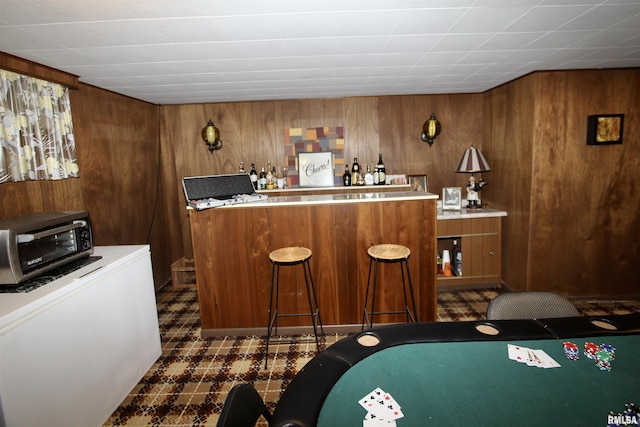 bar with a toaster, wooden walls, dark floors, refrigerator, and a bar