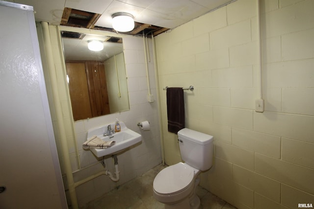 half bathroom with concrete block wall, a sink, and toilet