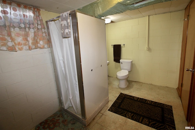 full bath with toilet, curtained shower, and concrete block wall