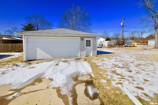 snow covered garage featuring a garage and fence