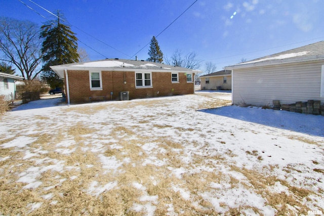 snow covered house featuring brick siding and central air condition unit