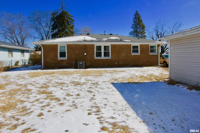 snow covered back of property featuring brick siding and central AC unit