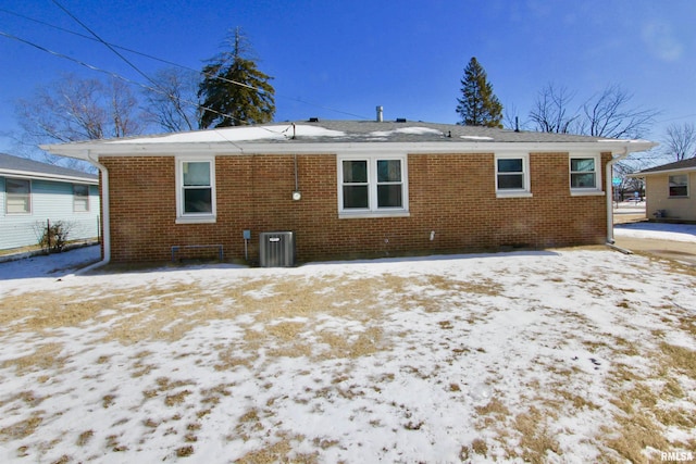 snow covered back of property featuring brick siding and cooling unit