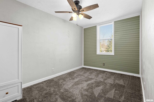 spare room featuring dark colored carpet, ceiling fan, and baseboards