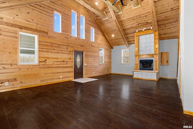 unfurnished living room with beam ceiling, wooden walls, wood finished floors, a tile fireplace, and wooden ceiling