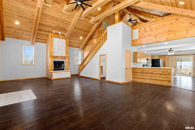 unfurnished living room with beam ceiling, dark wood-style flooring, a tile fireplace, and a ceiling fan