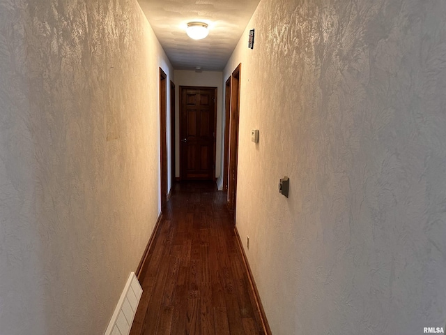 corridor with dark wood-style flooring, a textured wall, and baseboards