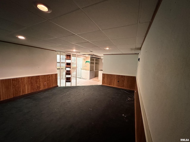 unfurnished room featuring a wainscoted wall, a drop ceiling, and wood walls