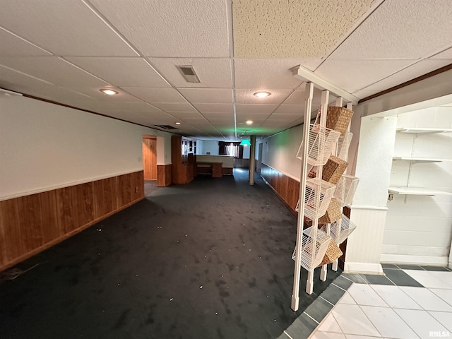 finished basement with visible vents, wainscoting, stairs, a paneled ceiling, and wood walls