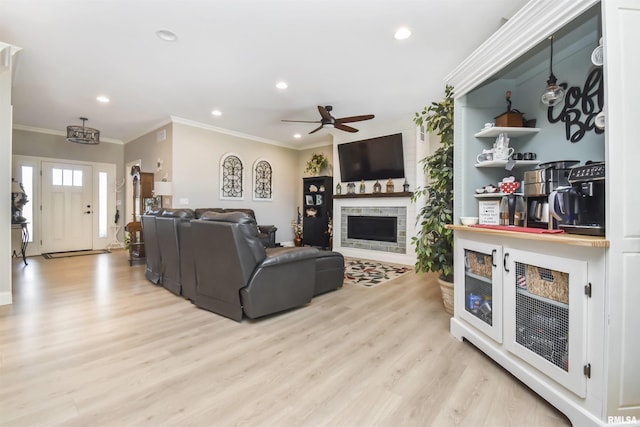 living area with a fireplace, recessed lighting, ornamental molding, a ceiling fan, and light wood-type flooring