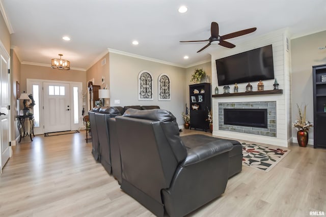 living room featuring light wood-style flooring, recessed lighting, ceiling fan with notable chandelier, a fireplace, and ornamental molding