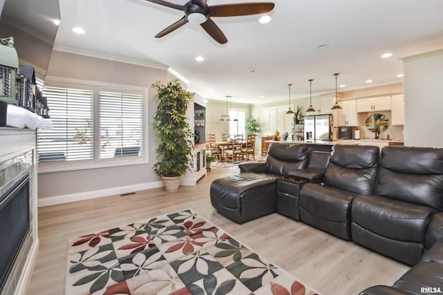 living room featuring ornamental molding, plenty of natural light, a fireplace, and light wood-style flooring