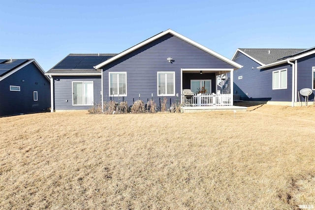 rear view of property with roof mounted solar panels and a lawn