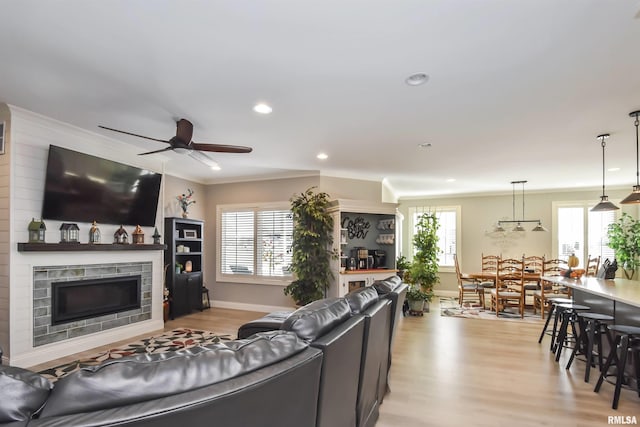 living room with crown molding, light wood-type flooring, a healthy amount of sunlight, and a fireplace