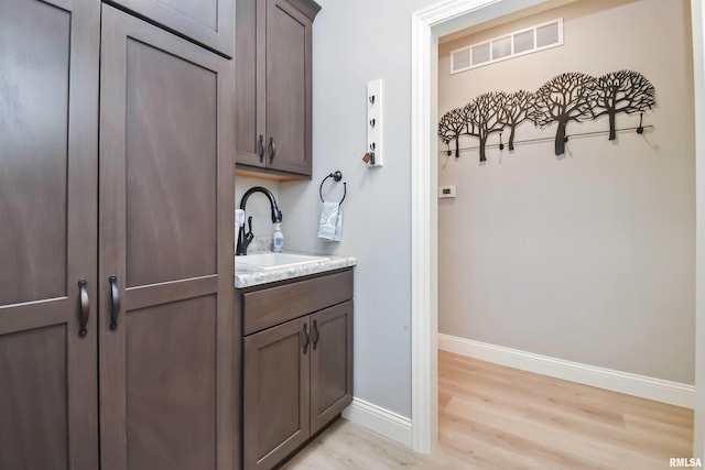 interior space featuring light wood-style floors, a sink, visible vents, and baseboards