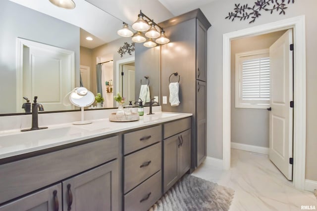 bathroom with marble finish floor, double vanity, a sink, and baseboards