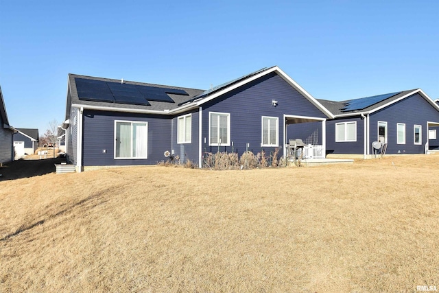 back of property featuring a yard and roof mounted solar panels