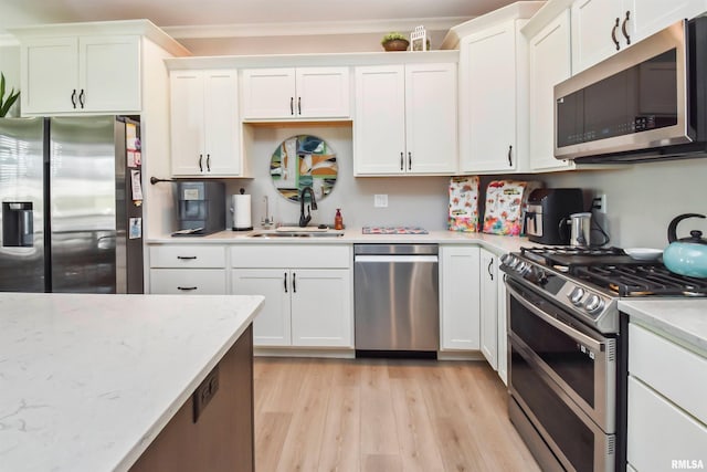 kitchen with stainless steel appliances, light wood-style flooring, ornamental molding, white cabinetry, and a sink