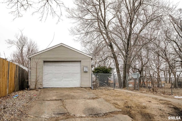 detached garage featuring concrete driveway and fence