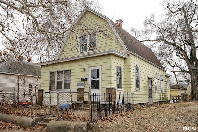 colonial inspired home featuring a fenced front yard, a chimney, a shingled roof, and a gambrel roof